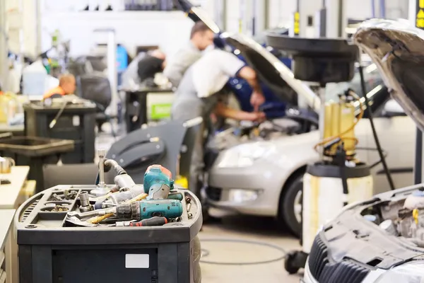 Auto repair shop scene with technicians working on cars; tools and equipment are arranged on a nearby workbench.